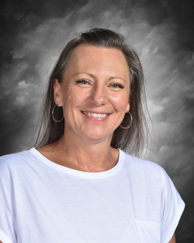 Smiling woman with hoop earrings and a white shirt against a cloudy gray background.