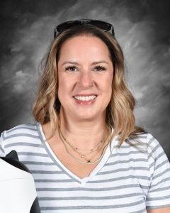 Woman smiling, wearing a striped shirt and sunglasses on her head, with a gray background.