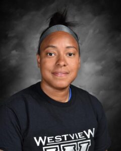 A woman with short hair wearing a black shirt with "Westview" printed on it, against a gray background.