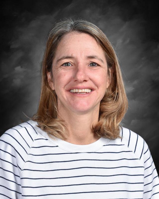 Woman with shoulder-length hair, wearing a white and navy striped sweater, smiles against a gray background.