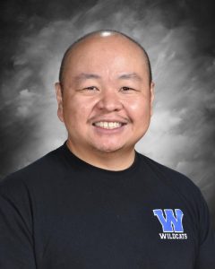 Smiling person wearing a black shirt with a "W Wildcats" logo, set against a cloudy gray background.