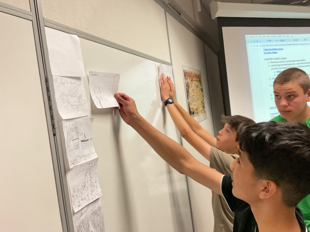 Students display their drawings on a classroom wall while engaging in a collaborative activity.
