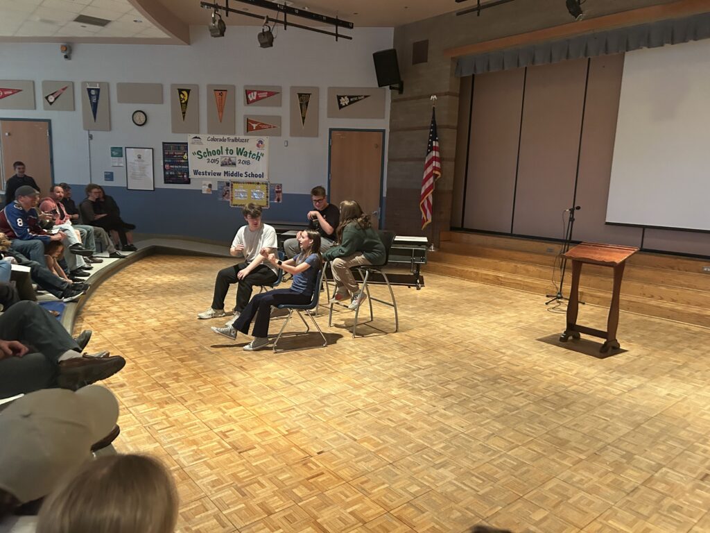 Students perform on stage at Westview Middle School during a school event, with an audience seated in the background.