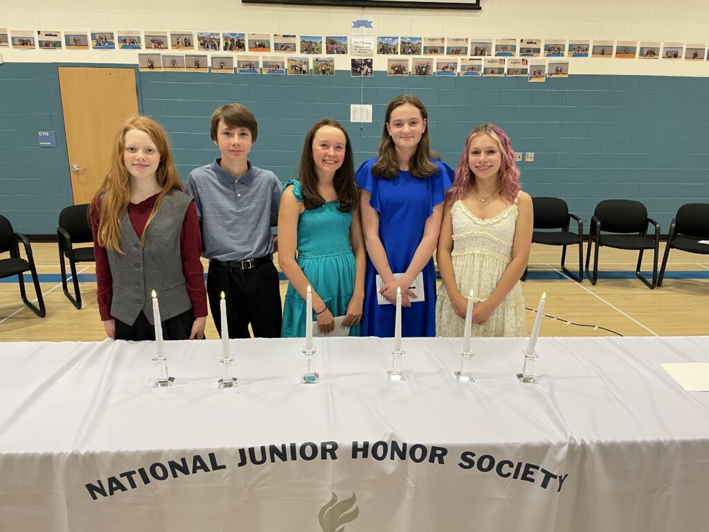 Five students stand at a table with lit candles, celebrating their induction into the National Junior Honor Society.