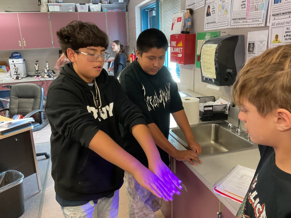 Students experiment with UV light in a classroom, observing its effects on their hands and discussing findings.