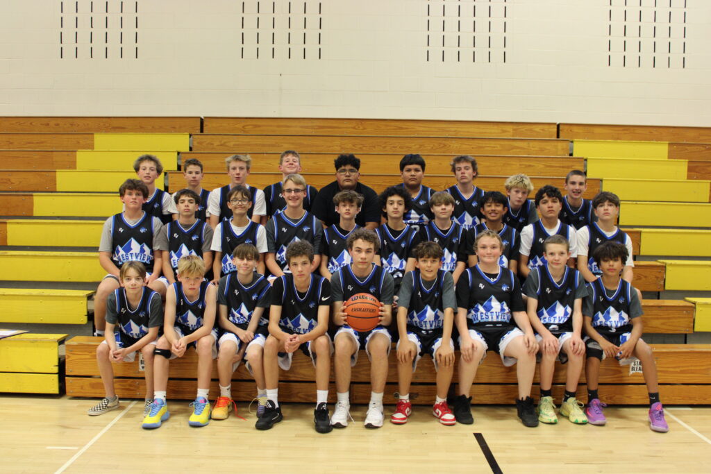 A youth basketball team poses on bleachers, wearing matching blue and black jerseys, with a basketball in front.