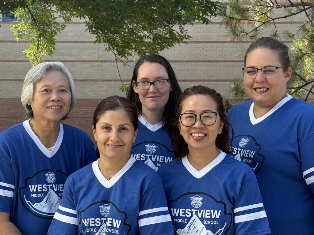 Five female staff members of Westview Middle School stand together, smiling, wearing matching blue school t-shirts.