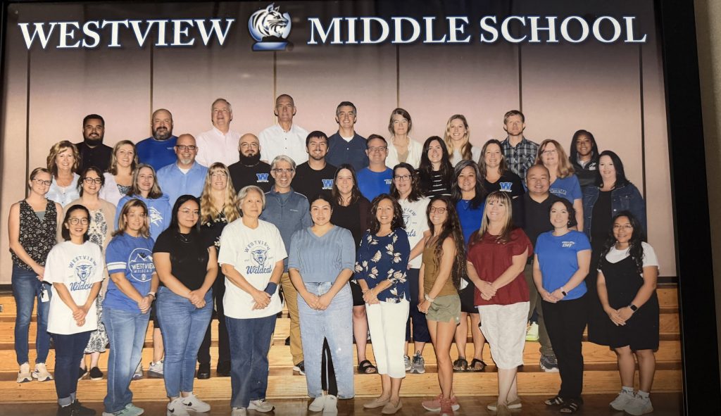Group photo of Westview Middle School staff, standing on stairs, wearing school colors and shirts, with a banner above.